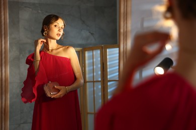 Photo of Beautiful woman with stylish bag getting ready near mirror indoors