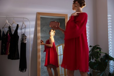 Photo of Beautiful woman with stylish bag getting ready near mirror indoors