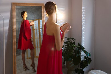 Photo of Beautiful woman with stylish bag getting ready near mirror indoors
