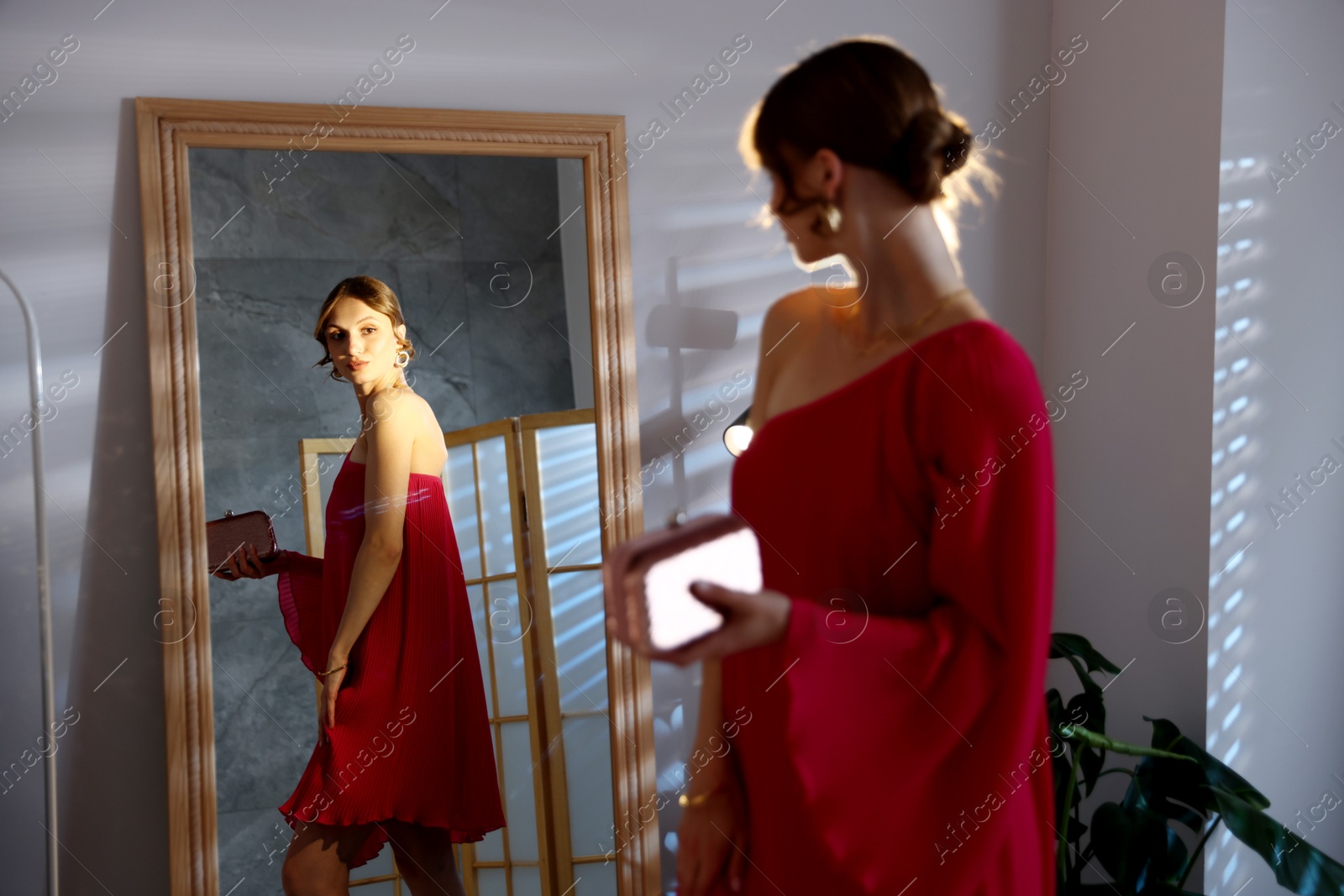 Beautiful woman with stylish bag getting ready near mirror indoors Photo of Beautiful woman with stylish bag getting ready near mirror indoors