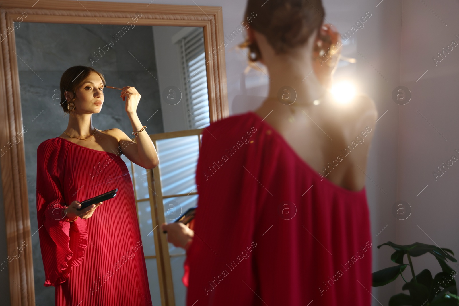 Photo of Beautiful woman applying makeup while getting ready near mirror indoors