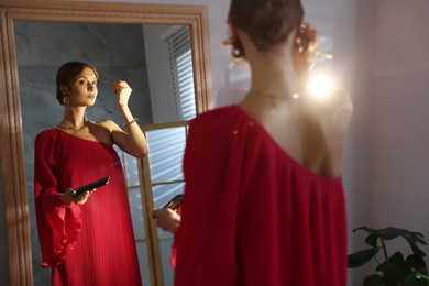 Photo of Beautiful woman applying makeup while getting ready near mirror indoors