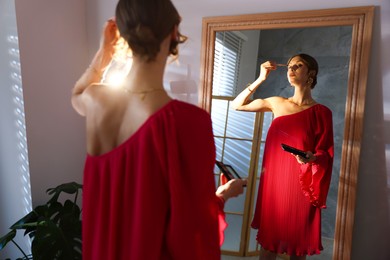 Photo of Beautiful woman applying makeup while getting ready near mirror indoors