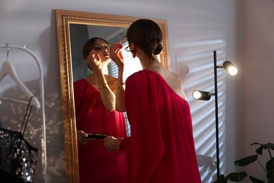 Photo of Beautiful woman applying makeup while getting ready near mirror indoors