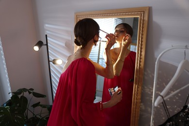Photo of Beautiful woman applying makeup while getting ready near mirror indoors