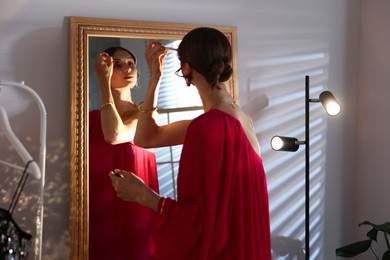 Photo of Beautiful woman applying makeup while getting ready near mirror indoors
