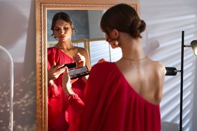 Photo of Beautiful woman applying makeup while getting ready near mirror indoors