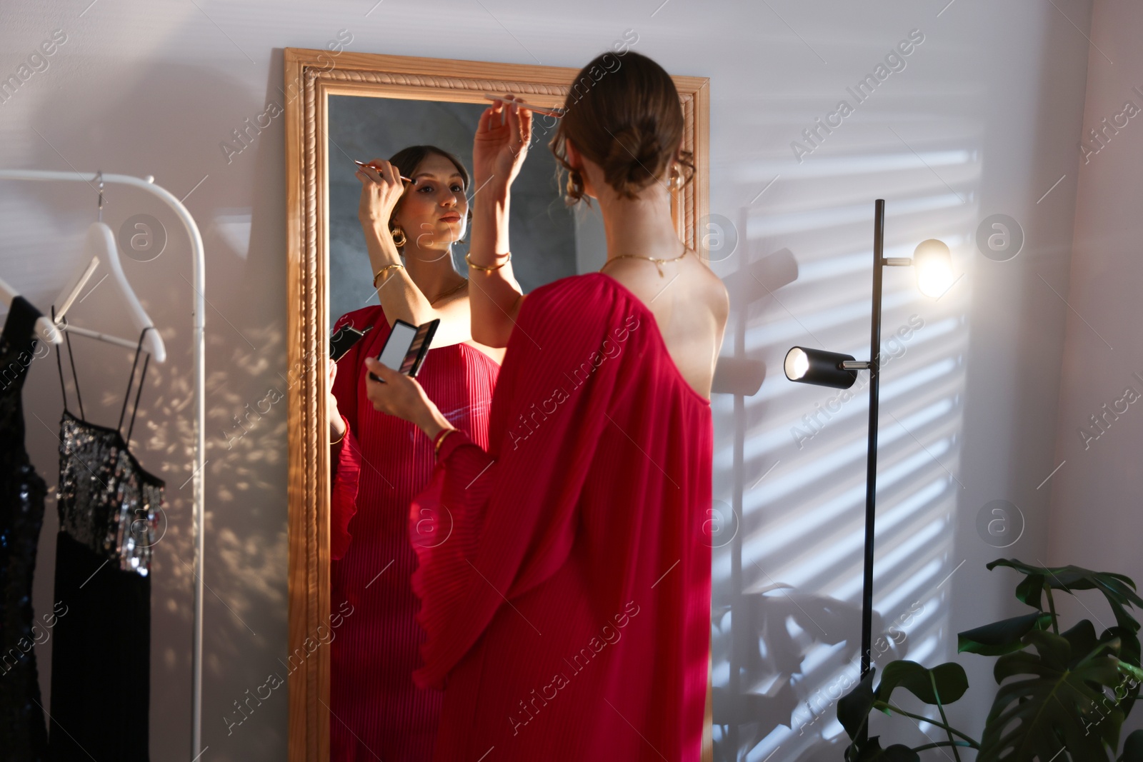 Photo of Beautiful woman applying makeup while getting ready near mirror indoors