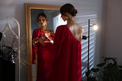 Photo of Beautiful woman applying makeup while getting ready near mirror indoors