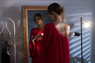 Photo of Beautiful woman applying makeup while getting ready near mirror indoors