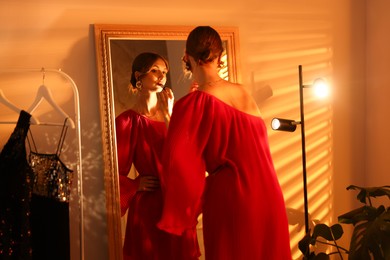 Photo of Beautiful woman applying lipstick while getting ready near mirror indoors