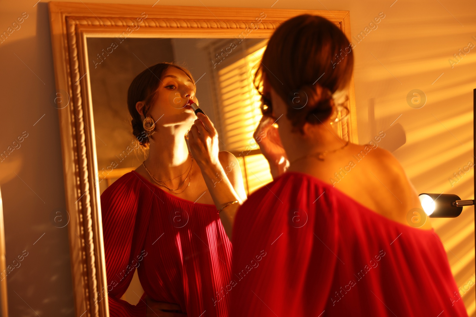 Beautiful woman applying lipstick while getting ready near mirror indoors Photo of Beautiful woman applying lipstick while getting ready near mirror indoors