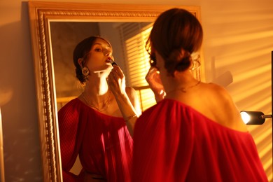 Photo of Beautiful woman applying lipstick while getting ready near mirror indoors