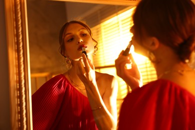 Photo of Beautiful woman applying lipstick while getting ready near mirror indoors