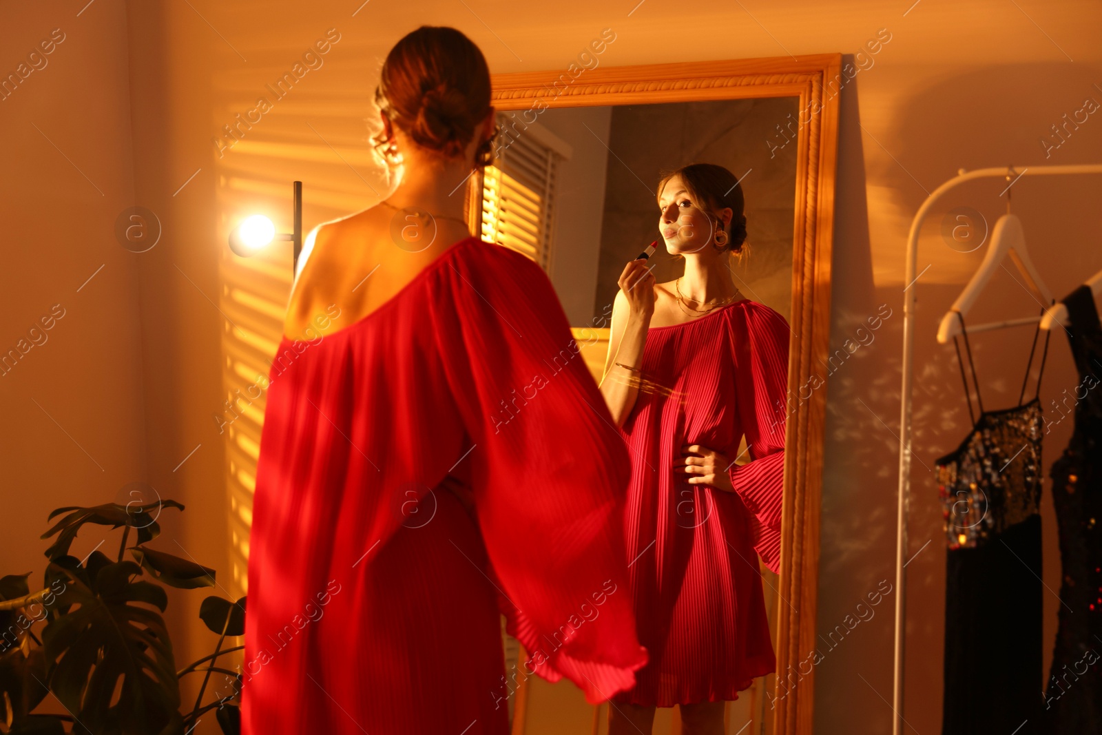 Photo of Beautiful woman applying lipstick while getting ready near mirror indoors