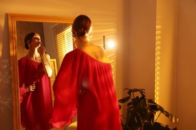 Photo of Beautiful woman applying lipstick while getting ready near mirror indoors