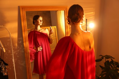Photo of Beautiful woman applying lipstick while getting ready near mirror indoors