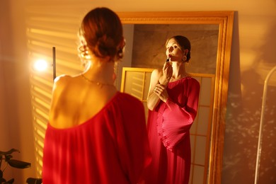 Photo of Beautiful woman applying lipstick while getting ready near mirror indoors