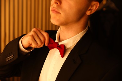 Photo of Man adjusting bow tie while getting ready indoors, closeup