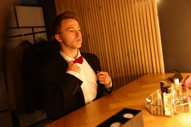 Photo of Man adjusting bow tie while getting ready at dressing table indoors