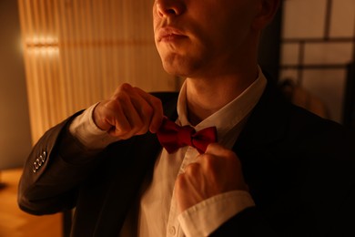 Photo of Man adjusting bow tie while getting ready indoors, closeup