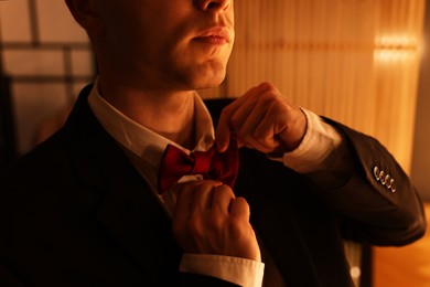 Photo of Man adjusting bow tie while getting ready indoors, closeup