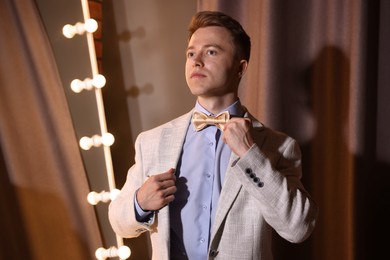 Photo of Handsome man adjusting bow tie while getting ready indoors