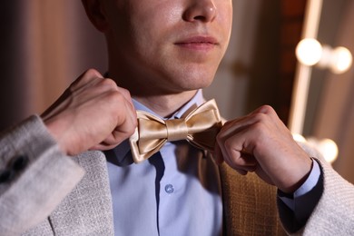 Photo of Man adjusting bow tie while getting ready indoors, closeup