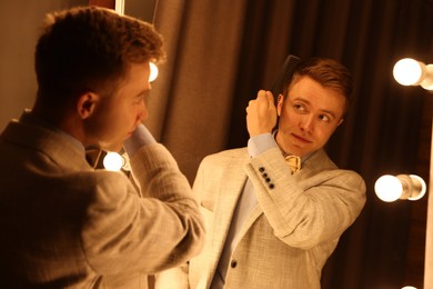 Photo of Handsome man brushing his hair while getting ready near mirror indoors
