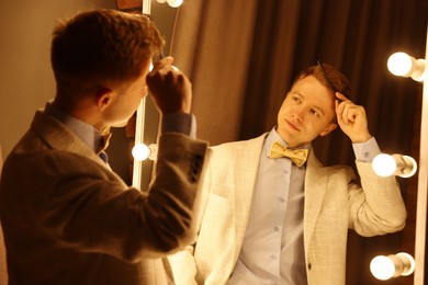 Photo of Handsome man brushing his hair while getting ready near mirror indoors
