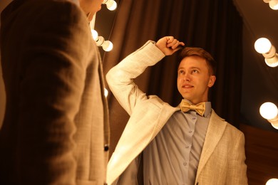 Photo of Handsome man brushing his hair while getting ready near mirror indoors