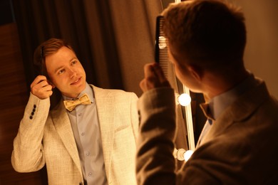Photo of Handsome man brushing his hair while getting ready near mirror indoors