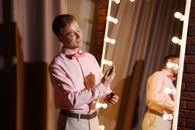 Photo of Handsome man spraying perfume while getting ready near mirror indoors