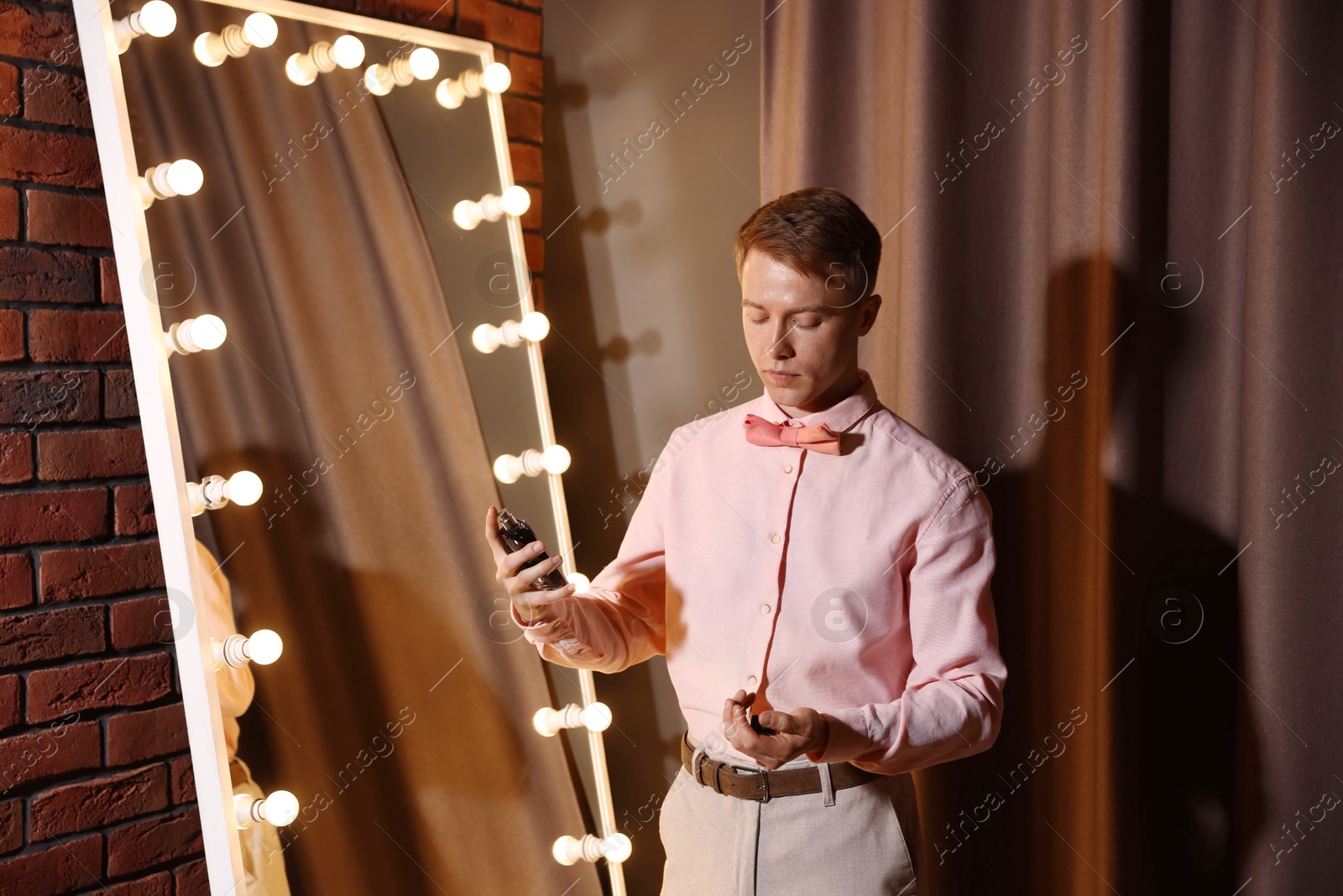 Handsome man spraying perfume while getting ready near mirror indoors Photo of Handsome man spraying perfume while getting ready near mirror indoors