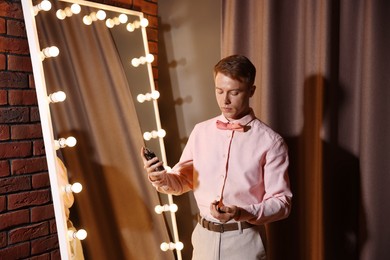 Photo of Handsome man spraying perfume while getting ready near mirror indoors