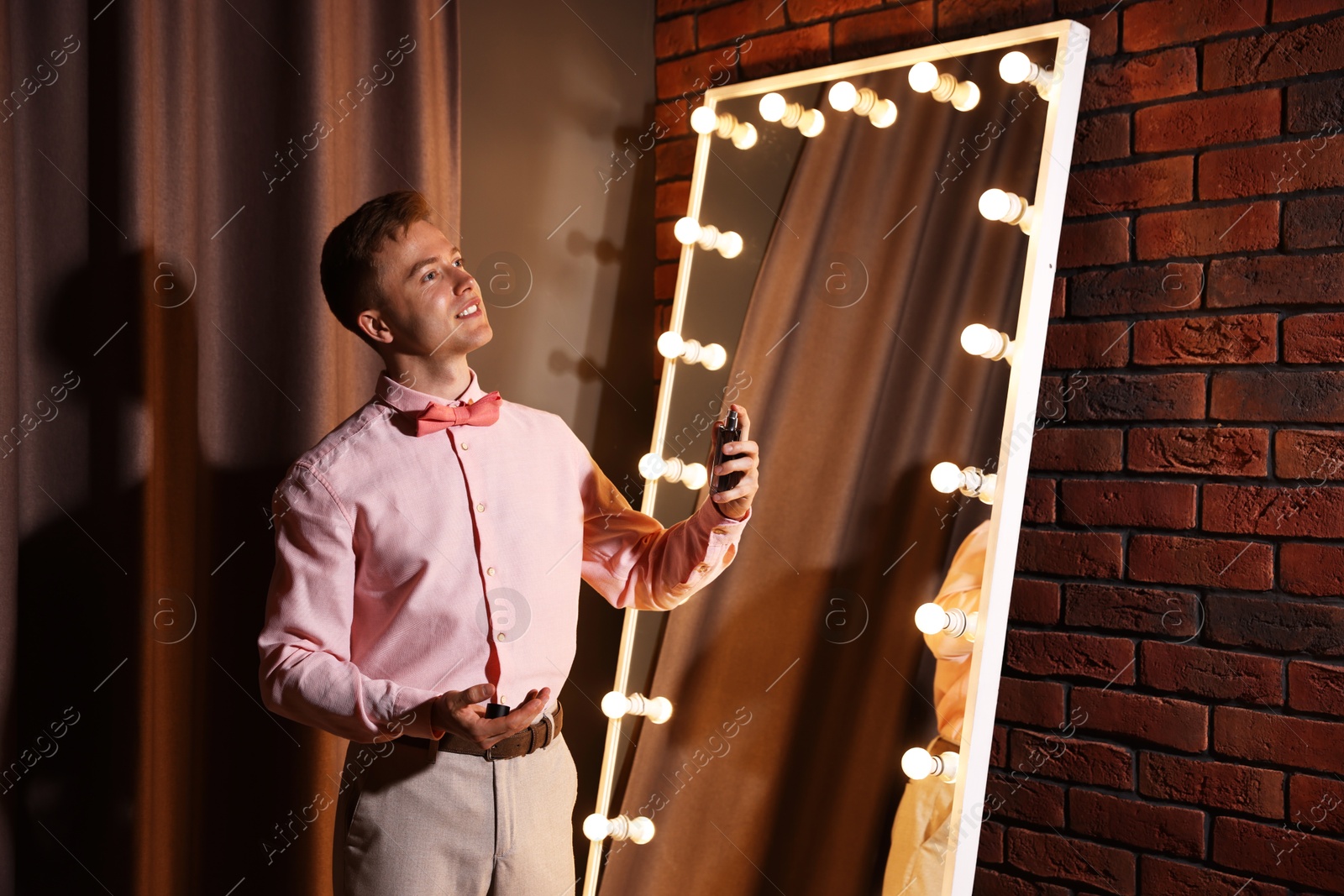 Handsome man spraying perfume while getting ready near mirror indoors Photo of Handsome man spraying perfume while getting ready near mirror indoors