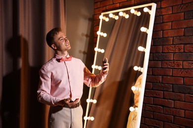 Photo of Handsome man spraying perfume while getting ready near mirror indoors
