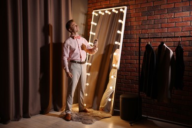 Photo of Handsome man spraying perfume while getting ready near mirror indoors