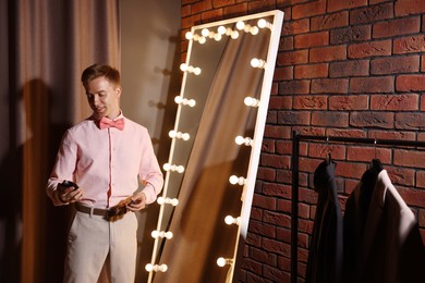 Photo of Handsome man with perfume getting ready near mirror indoors