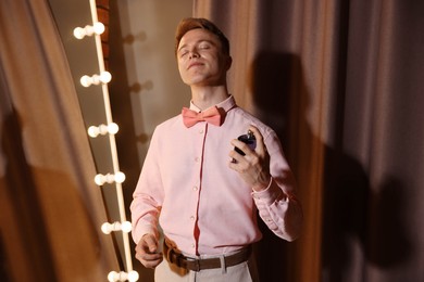 Photo of Handsome man spraying perfume while getting ready near mirror indoors