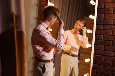 Photo of Handsome man brushing his hair while getting ready near mirror indoors