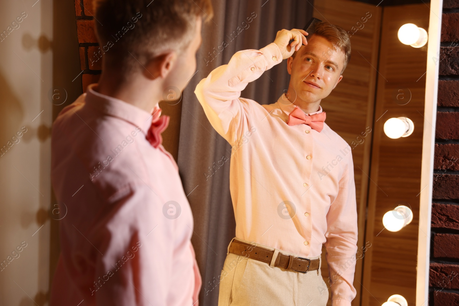 Handsome man brushing his hair while getting ready near mirror indoors Photo of Handsome man brushing his hair while getting ready near mirror indoors