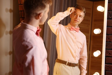 Photo of Handsome man brushing his hair while getting ready near mirror indoors