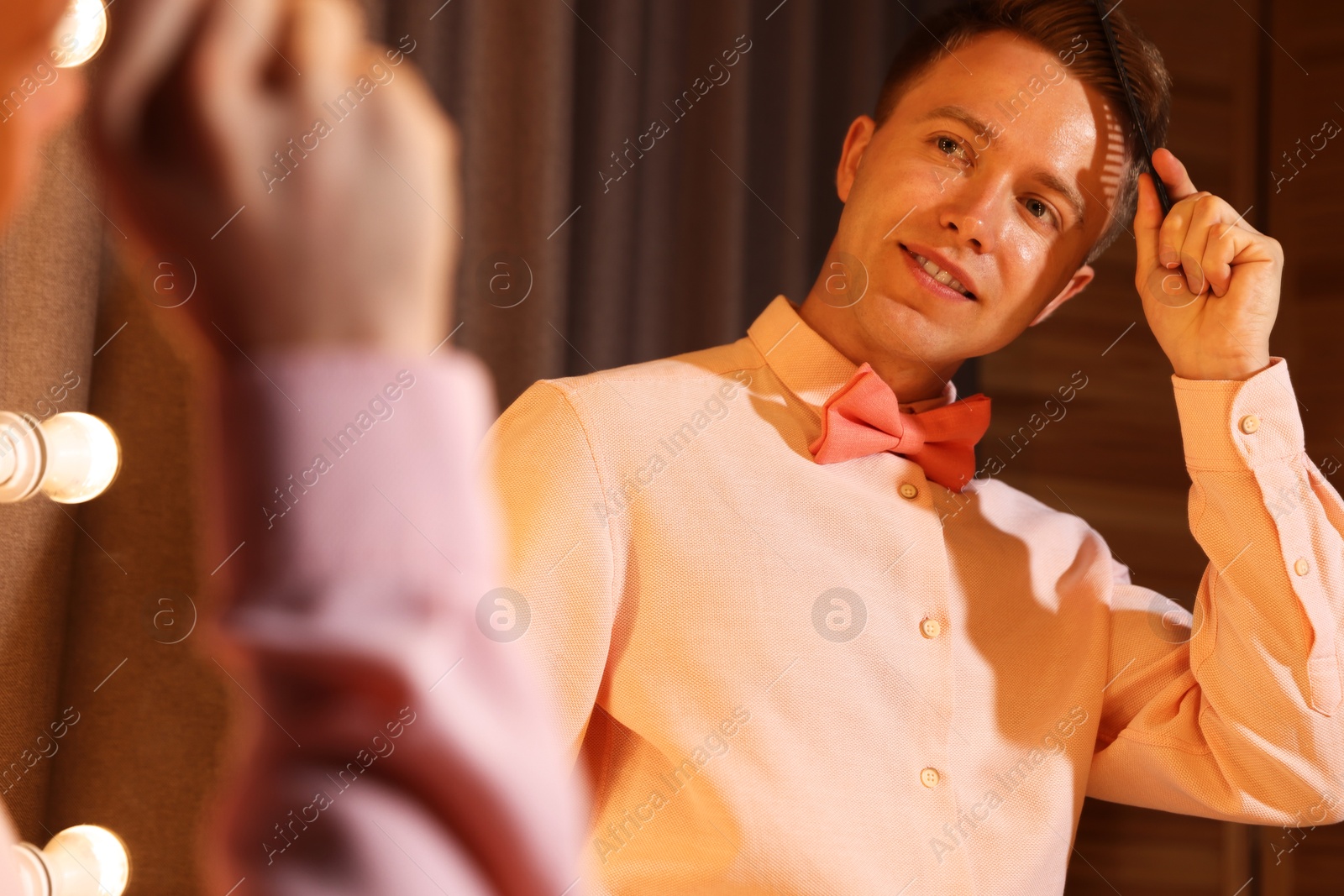 Handsome man brushing his hair while getting ready near mirror indoors Photo of Handsome man brushing his hair while getting ready near mirror indoors