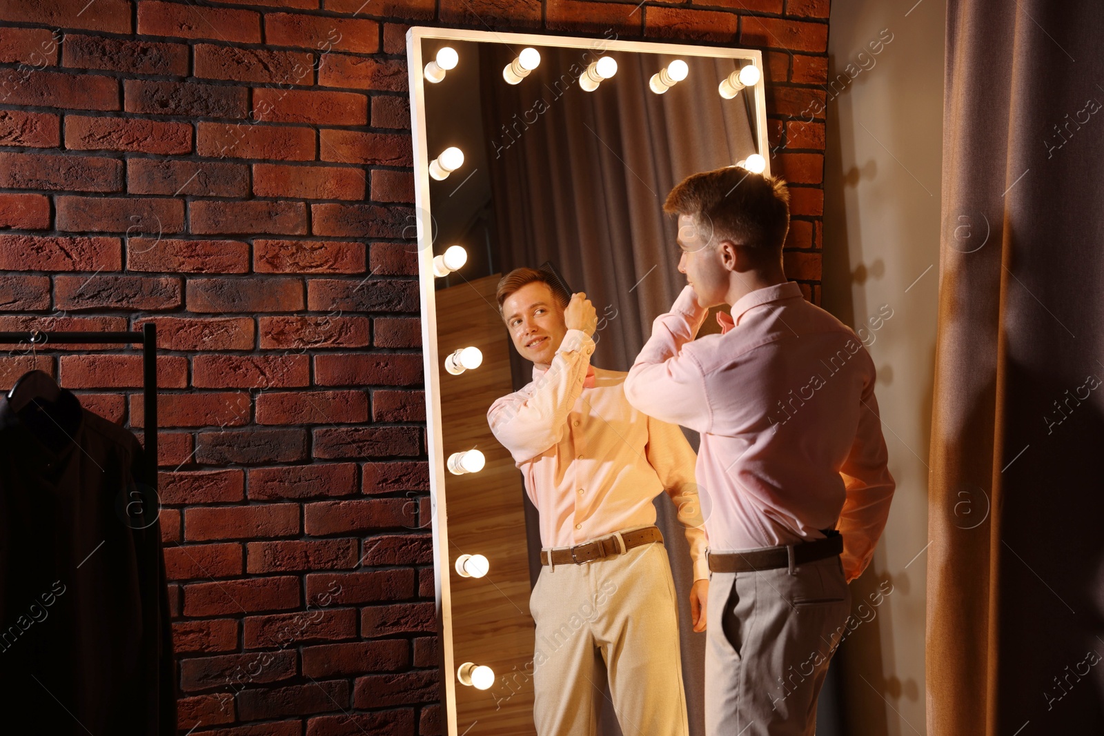 Handsome man brushing his hair while getting ready near mirror indoors Photo of Handsome man brushing his hair while getting ready near mirror indoors
