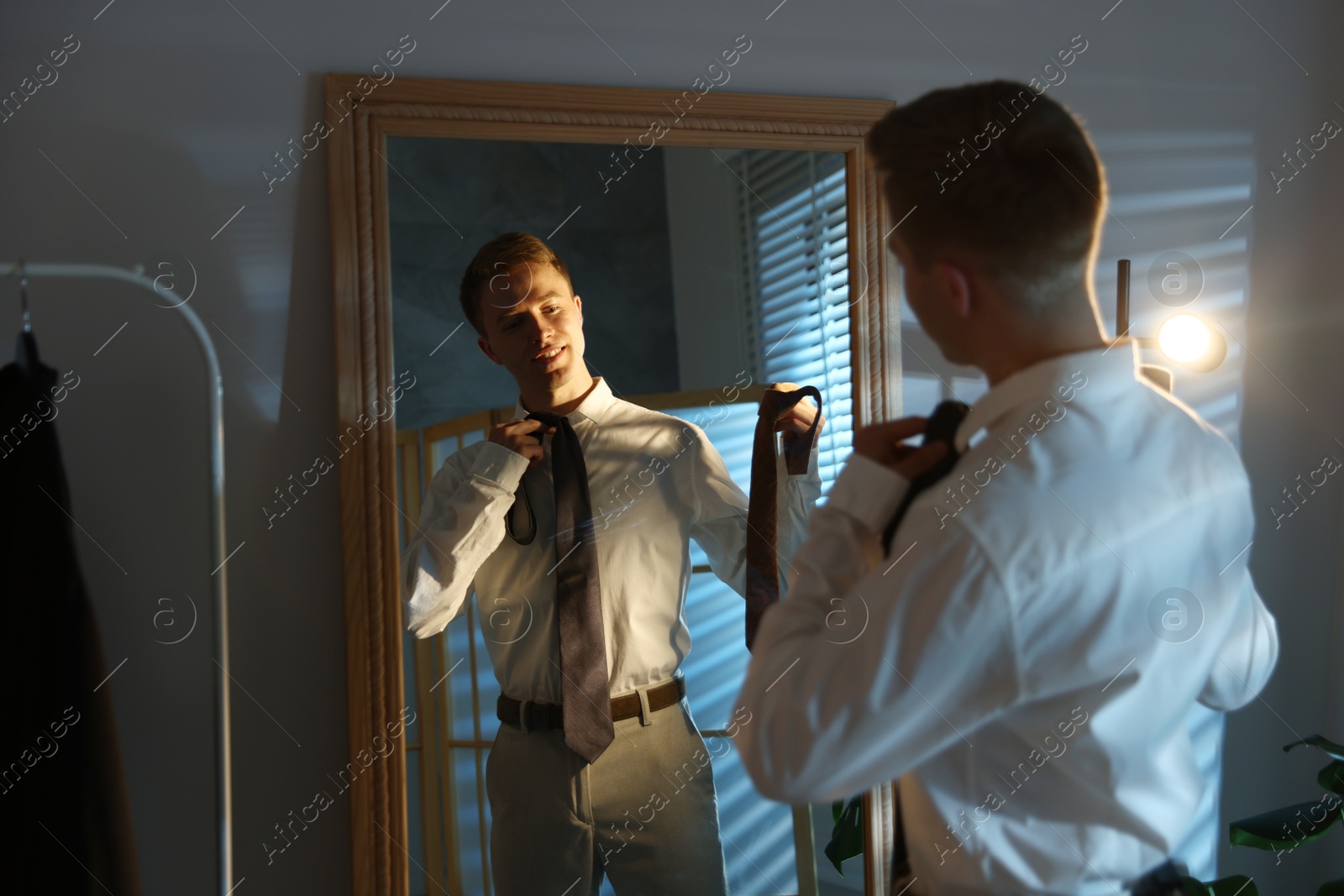 Man choosing neckties while getting ready near mirror indoors Photo of Man choosing neckties while getting ready near mirror indoors