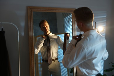 Photo of Man choosing neckties while getting ready near mirror indoors