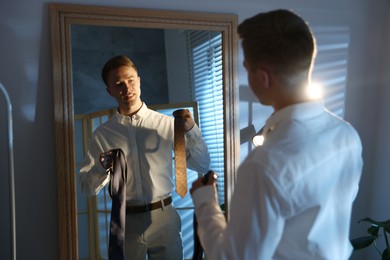 Photo of Man choosing neckties while getting ready near mirror indoors