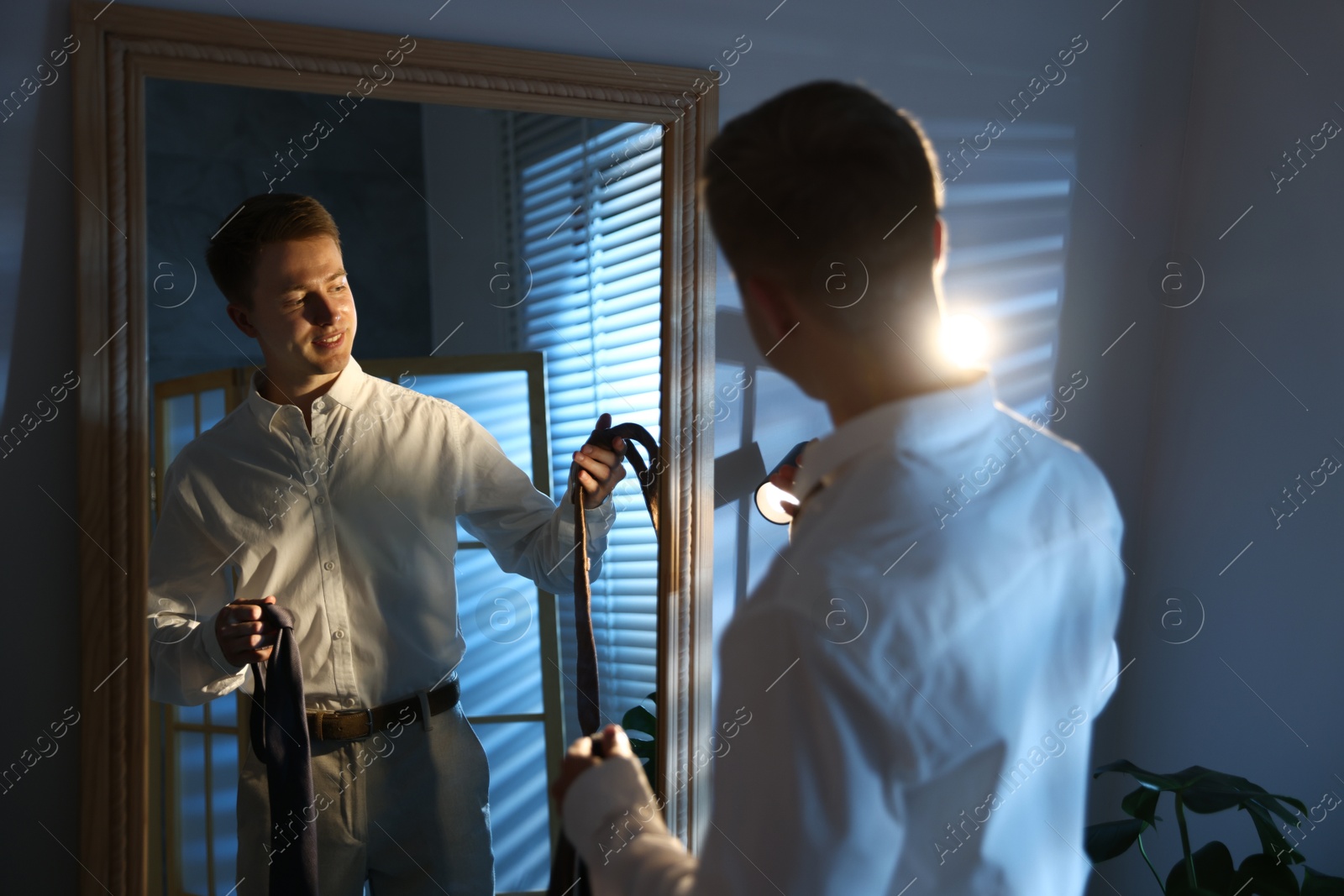 Man choosing neckties while getting ready near mirror indoors Photo of Man choosing neckties while getting ready near mirror indoors