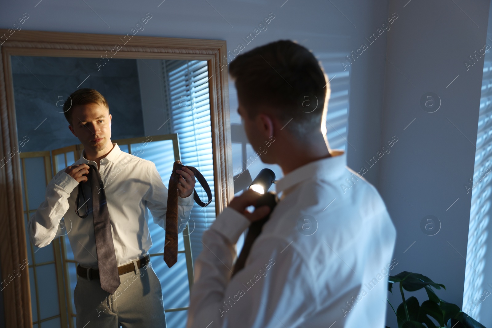 Man choosing neckties while getting ready near mirror indoors Photo of Man choosing neckties while getting ready near mirror indoors